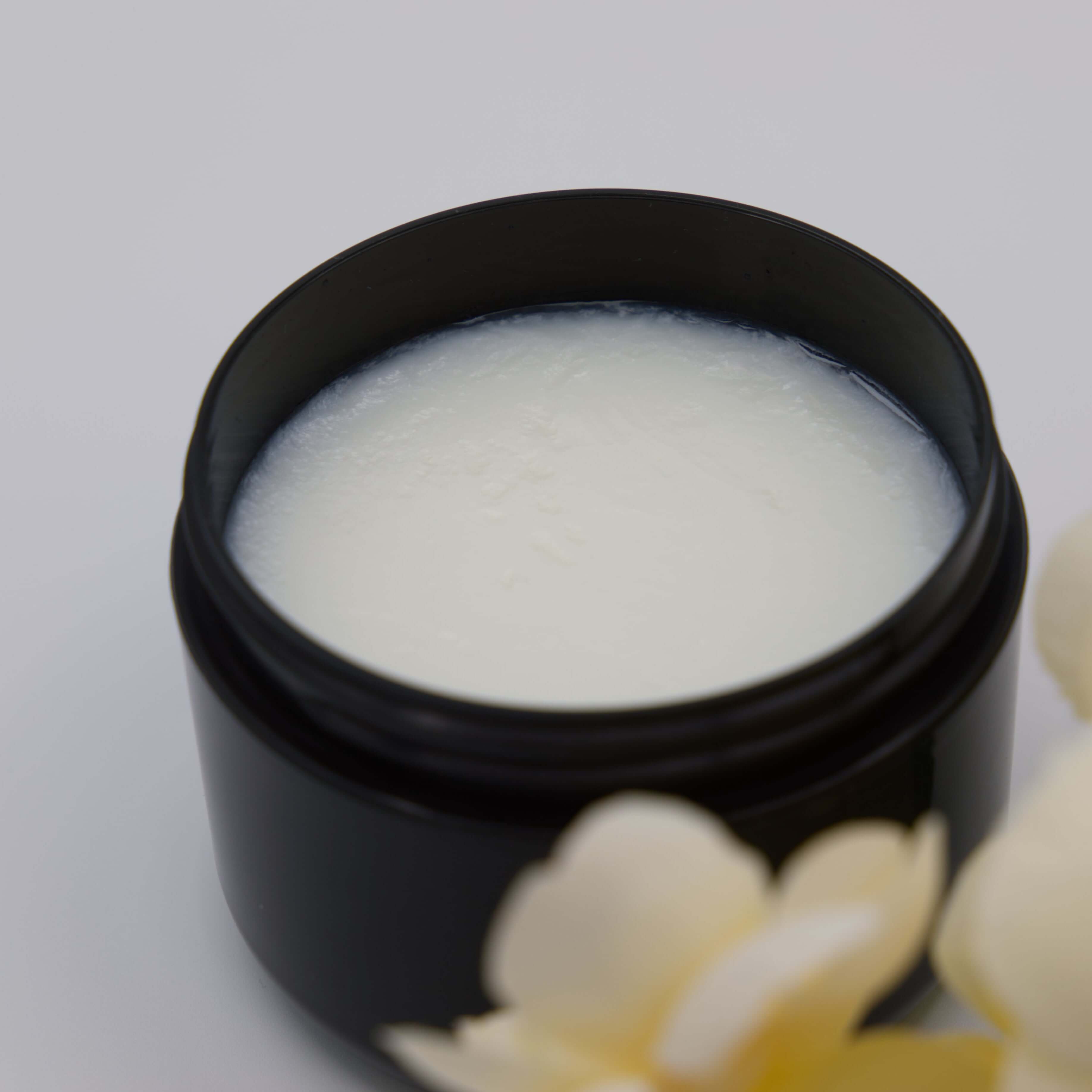 Black jar with white tallow cream inside, featuring a yellow flower design on a light gray background