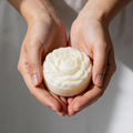 Hands holding a white flower-shaped bar of tallow against a neutral background
