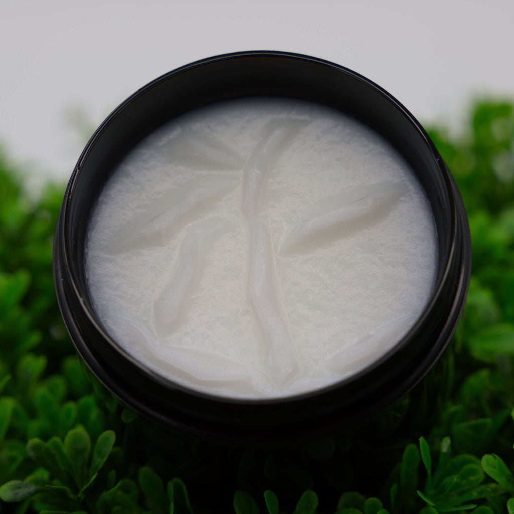 Black container with white tallow cream on a green leafy background