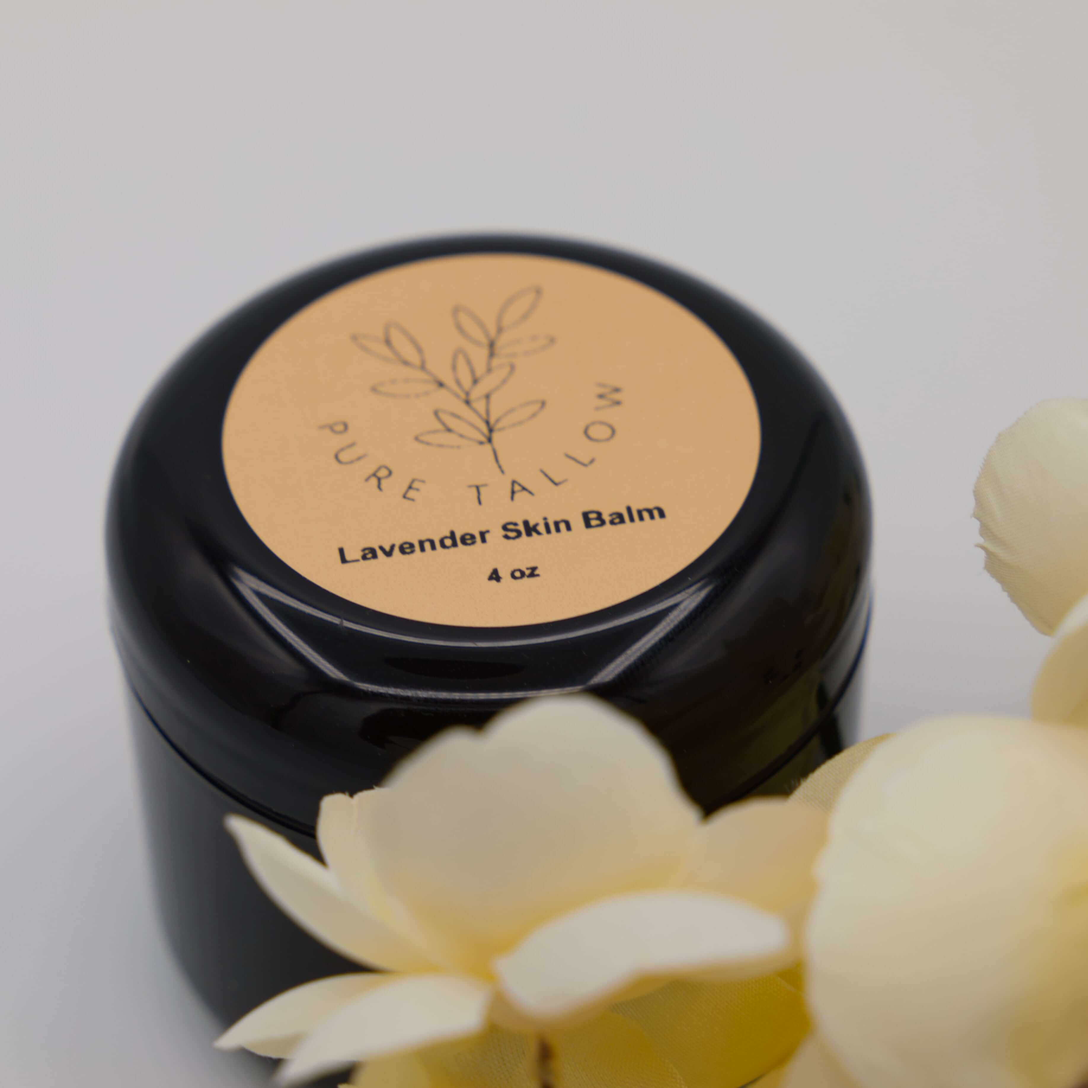 Black jar of Pure Tallow Lavender Skin Balm with flowers in the foreground