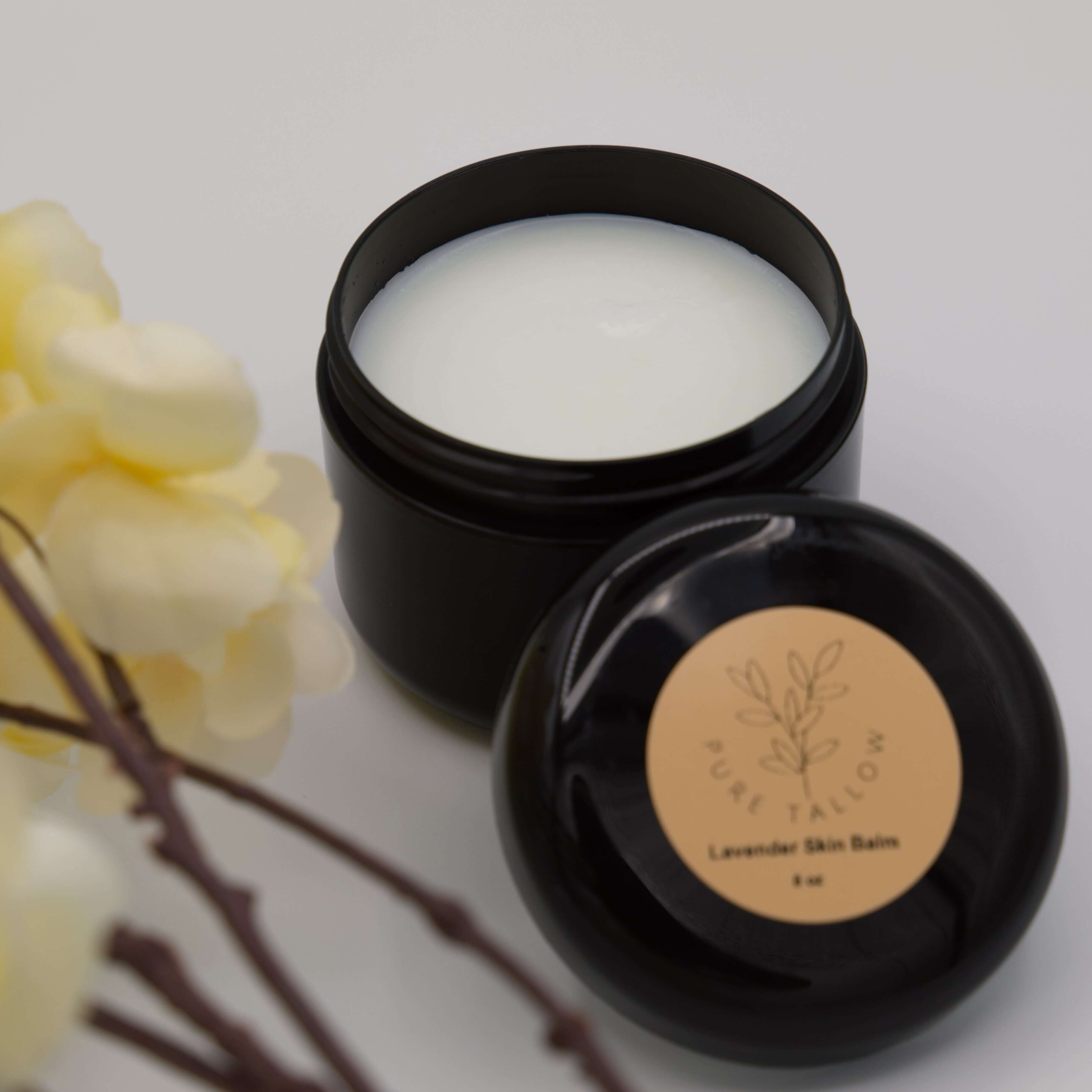 Black jar of lavender skin balm with a yellow flower on a white background
