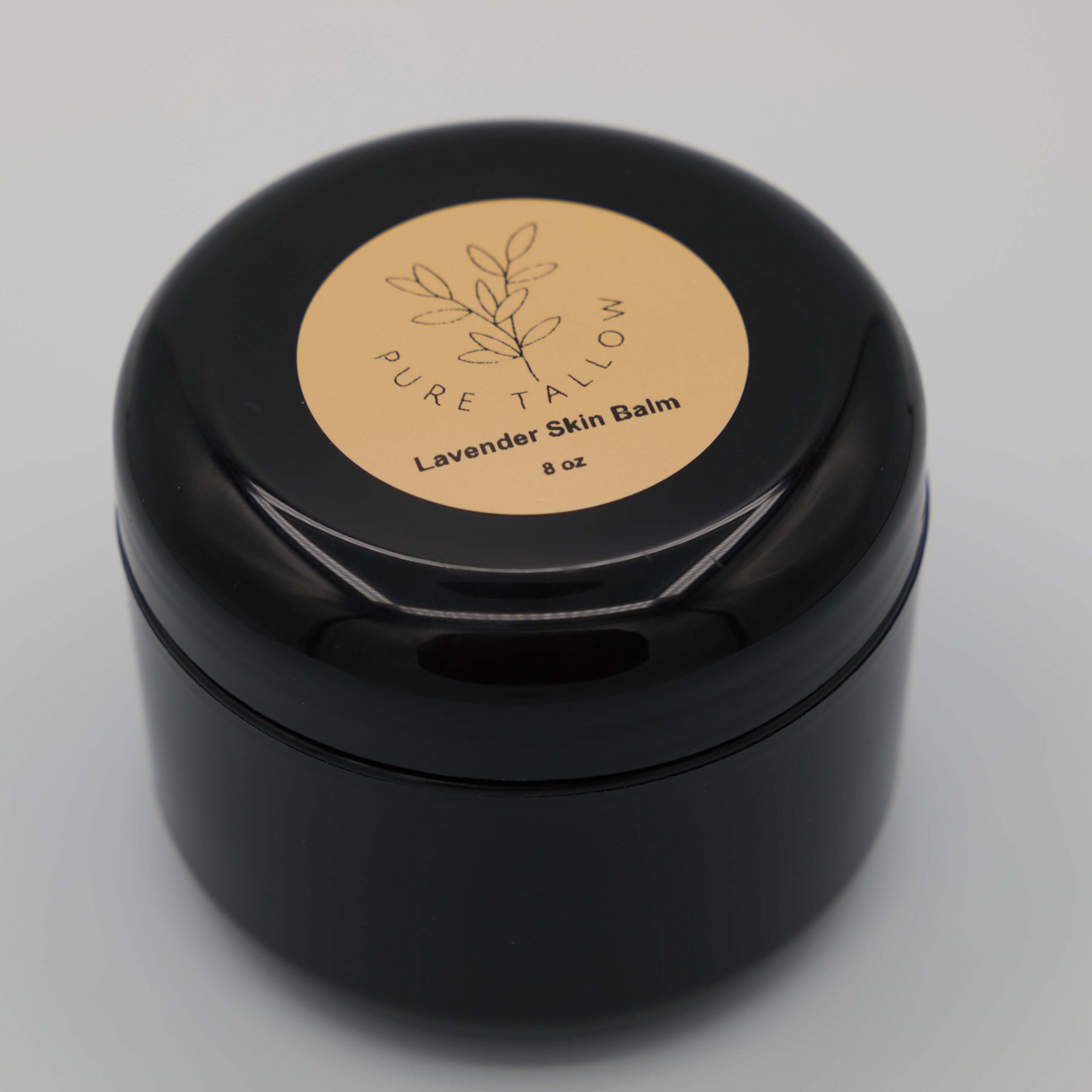 Black container of Pure Tallow Lavender Skin Balm on a light gray background