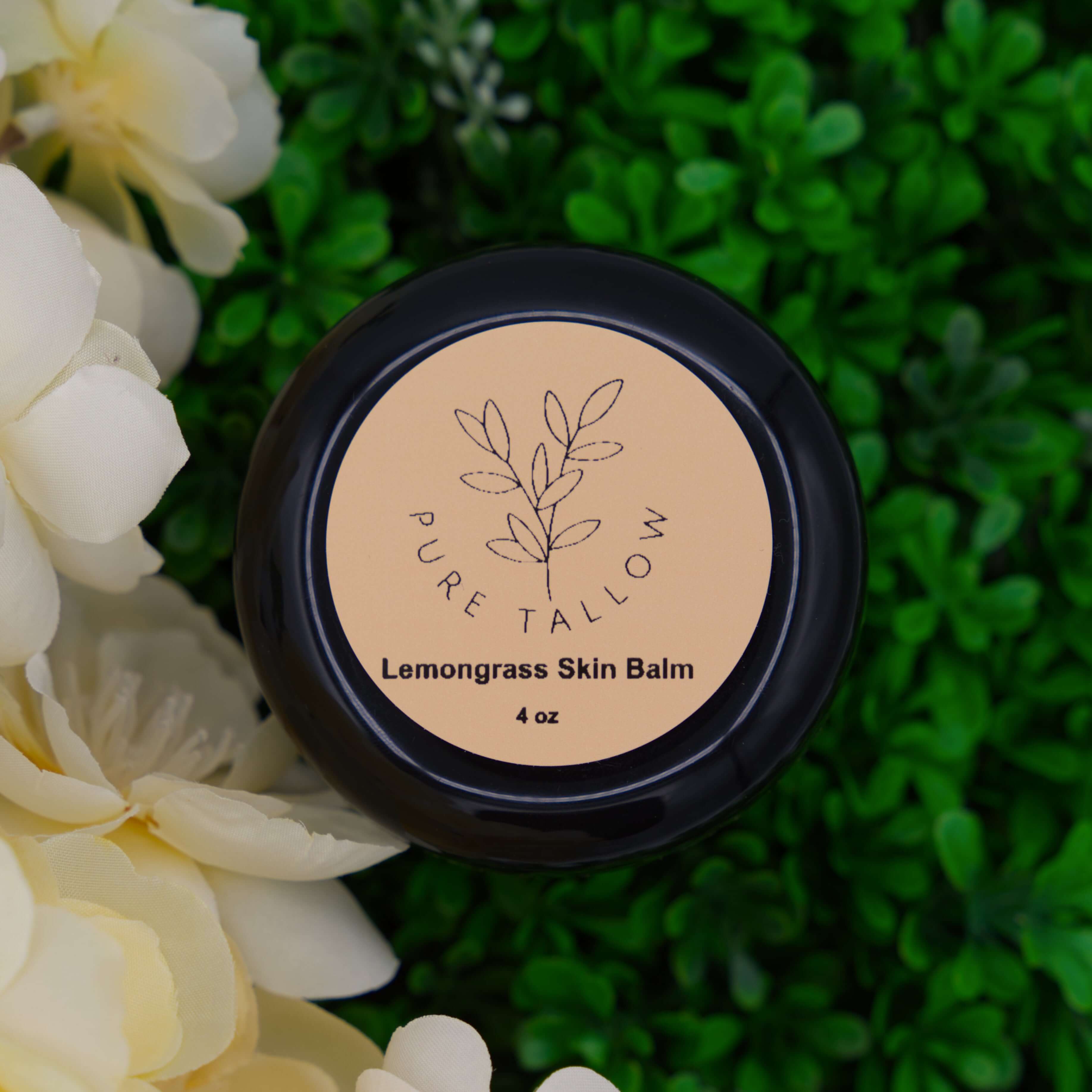 Lemongrass skin balm container with 'Pure Tallow' branding on a green leafy background and white/yellow flowers to the left