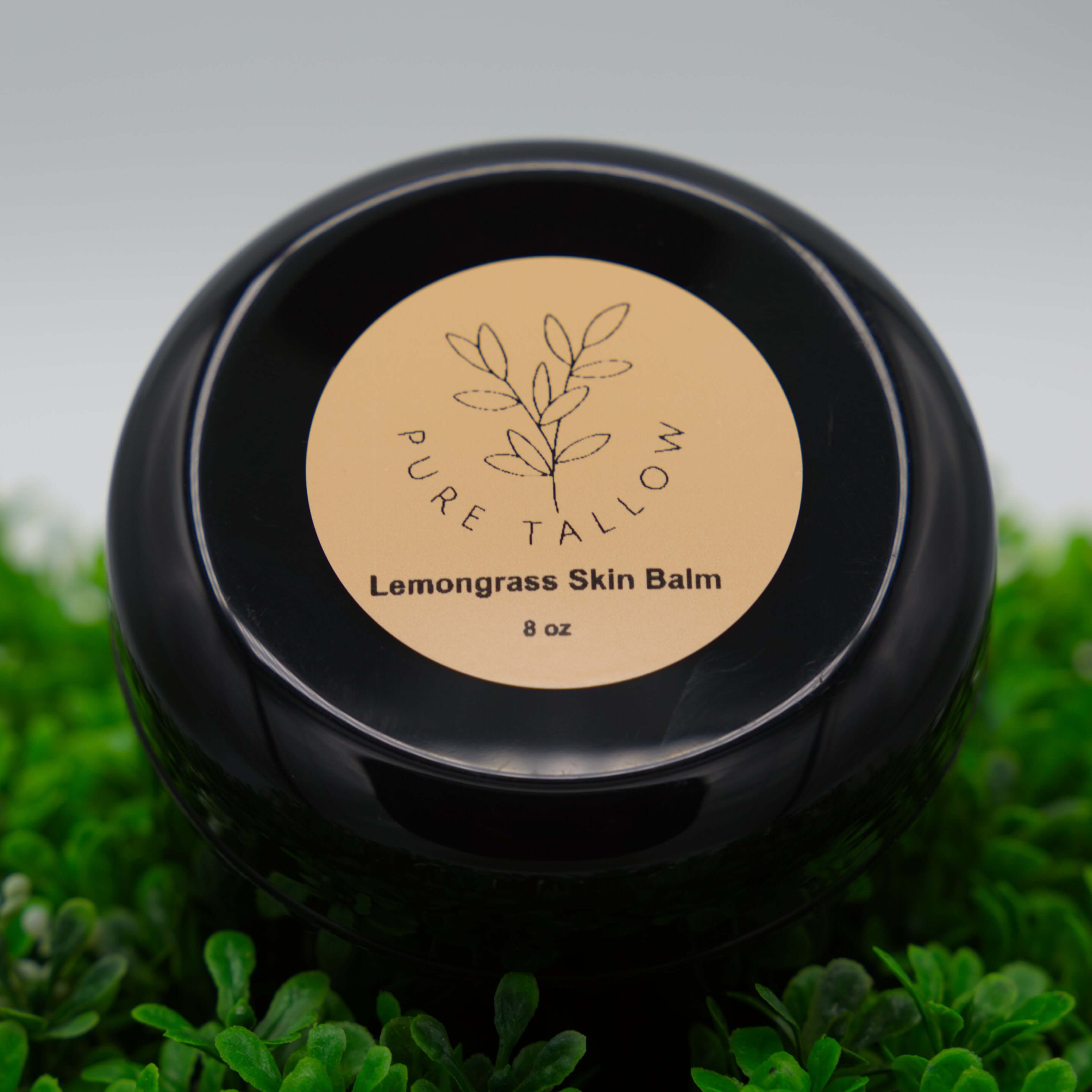 Black jar of Pure Tallow Lemongrass Skin Balm on a grass background