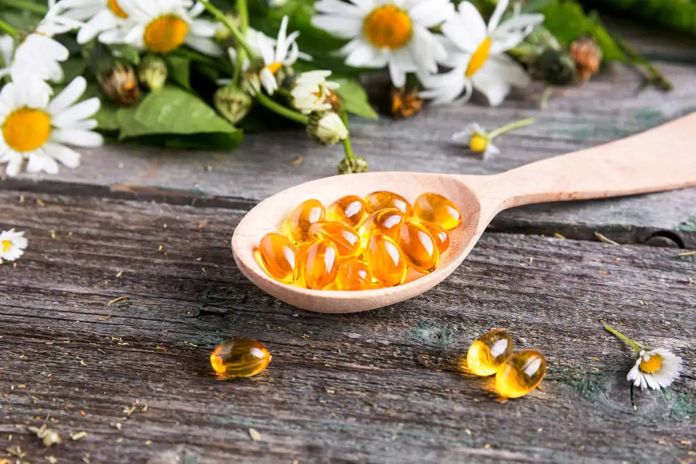 Wooden spoon with yellow capsules on a wooden surface with flowers in the background